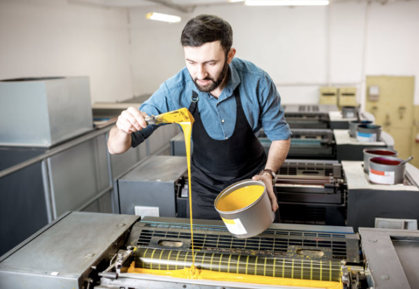 A pressman pours yellow ink into the ink duct of a sheet-fed offset press